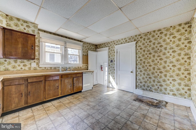 kitchen with light countertops, white dishwasher, a sink, and wallpapered walls