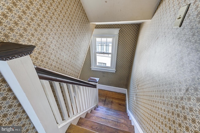 staircase with wallpapered walls, vaulted ceiling, and hardwood / wood-style flooring