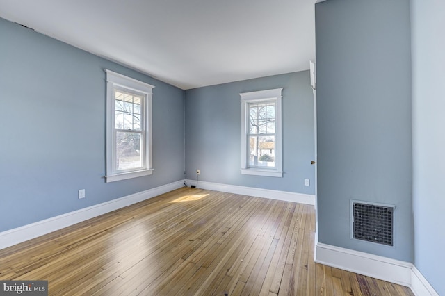 spare room featuring wood-type flooring, visible vents, and baseboards