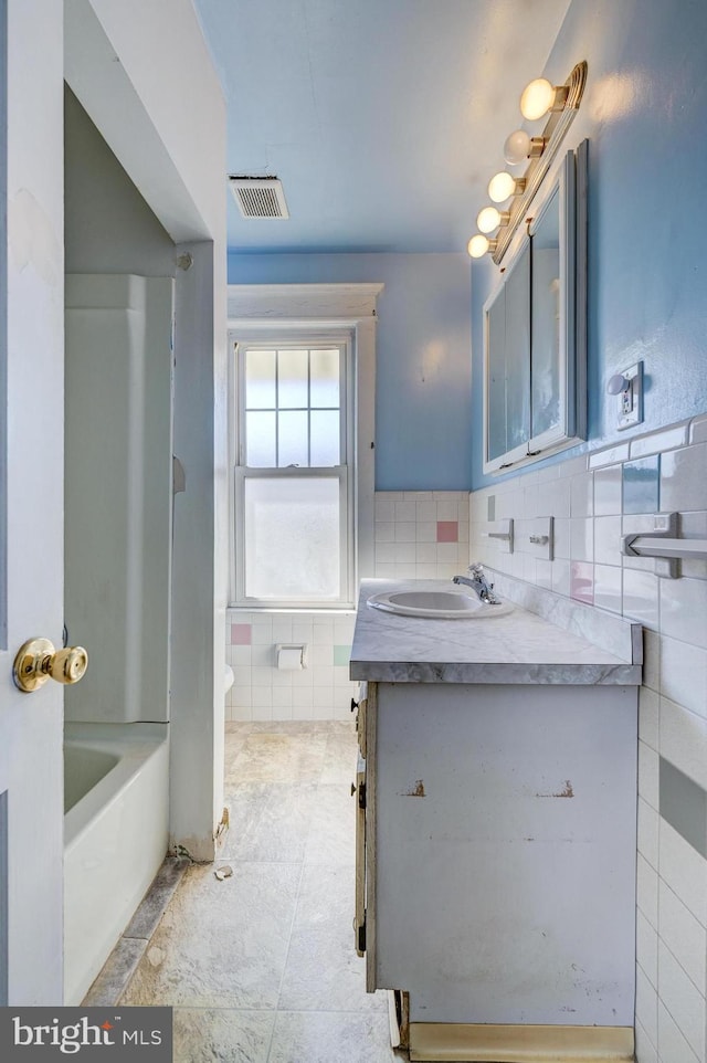 bathroom featuring visible vents, a tub to relax in, vanity, and tile walls