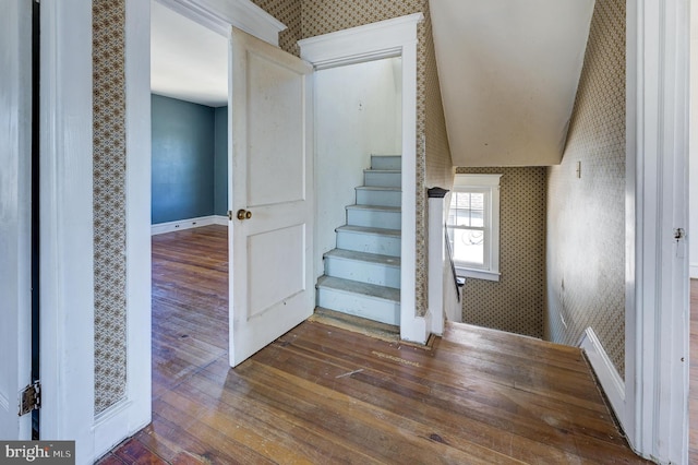 staircase featuring hardwood / wood-style flooring, vaulted ceiling, baseboards, and wallpapered walls