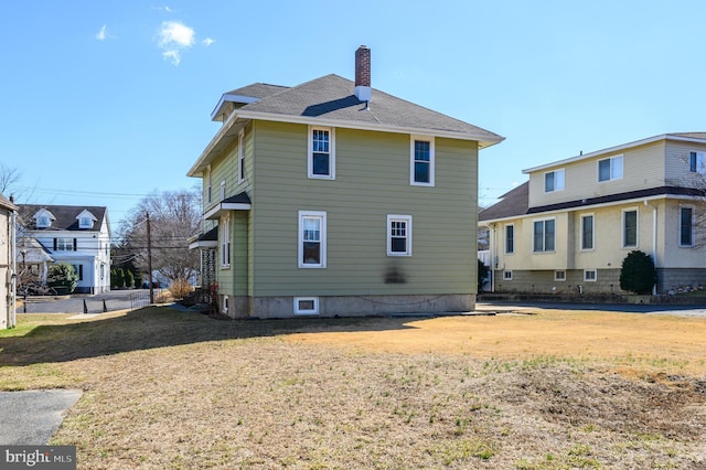 back of property with a chimney and a lawn