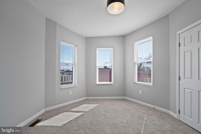 unfurnished room with a wealth of natural light, baseboards, visible vents, and carpet flooring