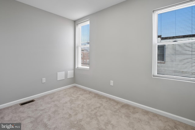 carpeted spare room with baseboards, visible vents, and a wealth of natural light