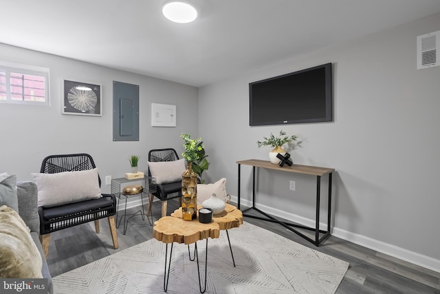 living area featuring electric panel, visible vents, baseboards, and wood finished floors