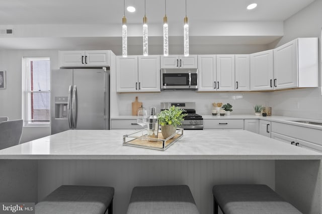 kitchen with decorative light fixtures, appliances with stainless steel finishes, white cabinets, and a kitchen breakfast bar