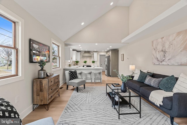 living area with recessed lighting, baseboards, light wood-style floors, and high vaulted ceiling