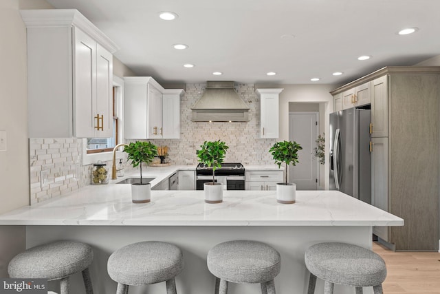 kitchen featuring light stone countertops, a peninsula, custom exhaust hood, stainless steel appliances, and a sink