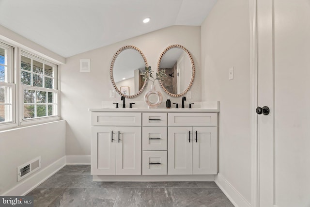 bathroom featuring a sink, visible vents, lofted ceiling, and baseboards