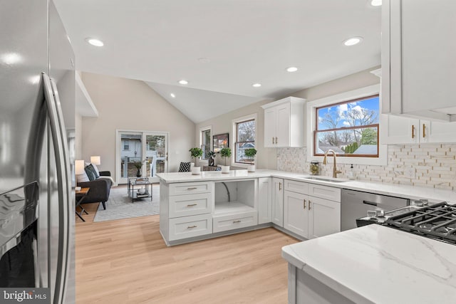 kitchen featuring light wood finished floors, vaulted ceiling, a peninsula, stainless steel appliances, and a sink