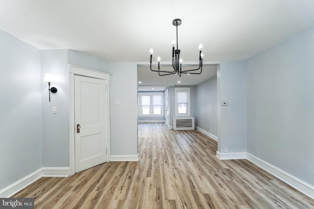 unfurnished dining area featuring baseboards, a notable chandelier, and light wood finished floors