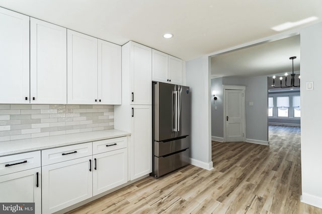 kitchen featuring high quality fridge, light wood-type flooring, backsplash, and white cabinets