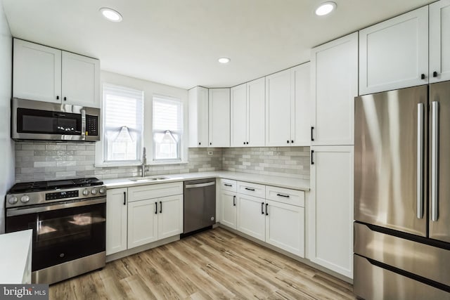 kitchen with appliances with stainless steel finishes, light countertops, light wood-style floors, white cabinetry, and a sink