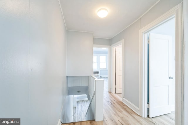 hallway with baseboards, an upstairs landing, and light wood-style floors