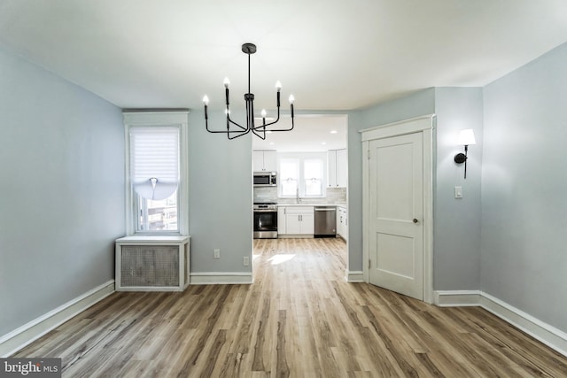 unfurnished dining area featuring a chandelier, radiator heating unit, light wood-type flooring, and baseboards