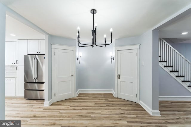 unfurnished dining area with stairs, light wood-type flooring, an inviting chandelier, and baseboards