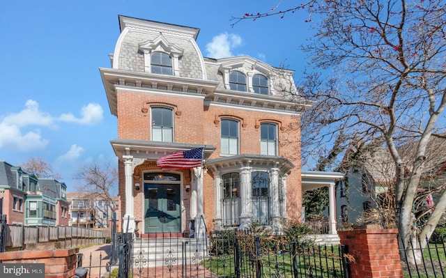 second empire-style home featuring mansard roof, brick siding, a fenced front yard, and a gate