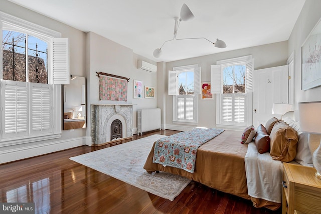 bedroom with baseboards, radiator, wood finished floors, a wall mounted air conditioner, and a fireplace