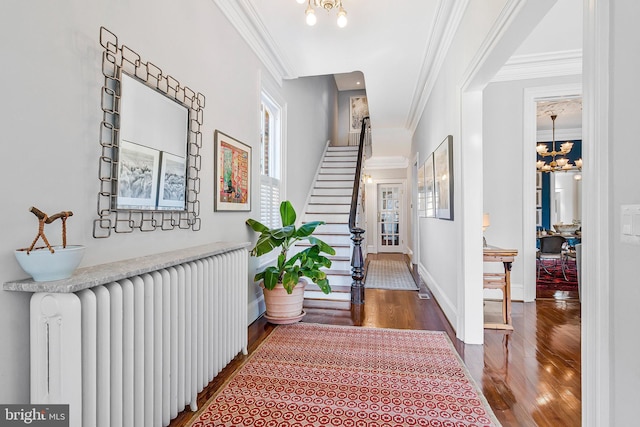 hall with a notable chandelier, wood finished floors, radiator heating unit, and ornamental molding