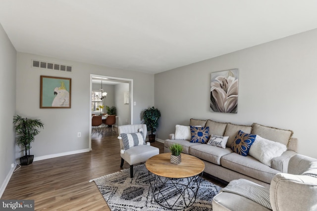 living area with baseboards, wood finished floors, visible vents, and an inviting chandelier