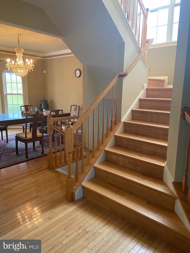 stairway featuring hardwood / wood-style flooring, ornamental molding, and an inviting chandelier