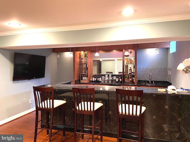 bar with dark wood-style floors, tasteful backsplash, ornamental molding, wet bar, and baseboards