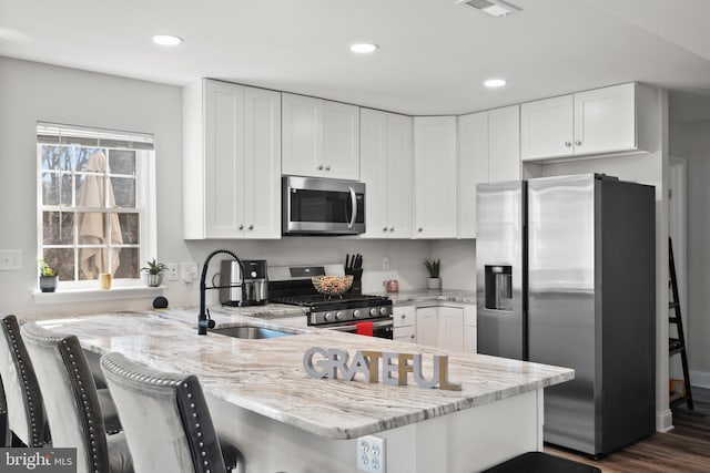 kitchen featuring appliances with stainless steel finishes, a peninsula, light stone countertops, white cabinetry, and a sink