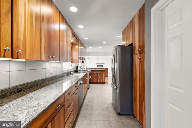 kitchen featuring brown cabinets, light tile patterned floors, backsplash, freestanding refrigerator, and a sink