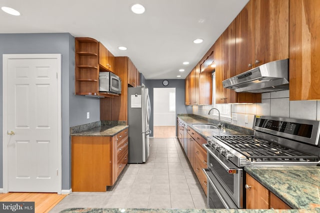 kitchen with under cabinet range hood, appliances with stainless steel finishes, brown cabinets, and a sink