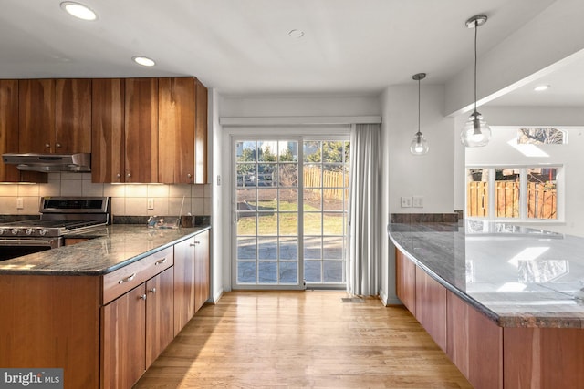 kitchen featuring dark stone counters, decorative backsplash, a peninsula, under cabinet range hood, and gas stove