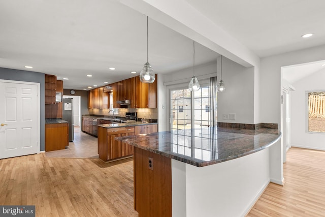 kitchen featuring a peninsula, light wood finished floors, stainless steel gas range oven, and brown cabinets