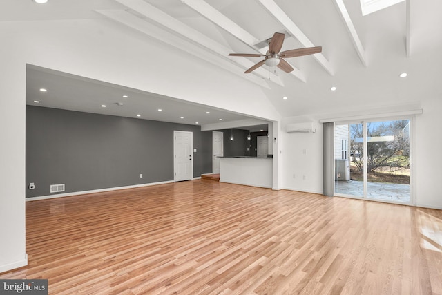 unfurnished living room with a wall unit AC, a skylight, light wood finished floors, and beam ceiling