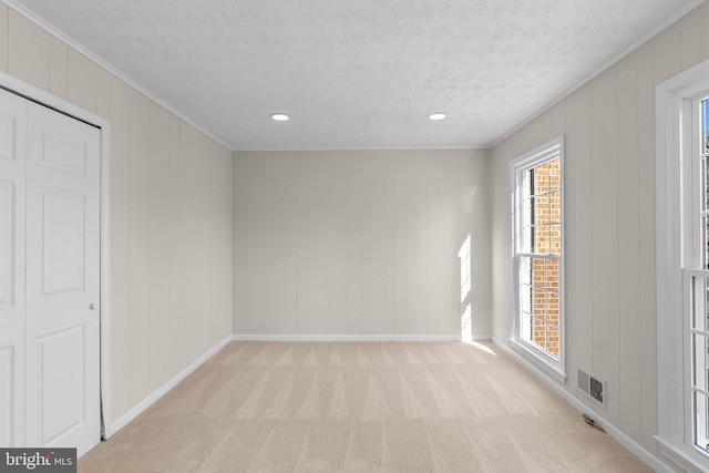 unfurnished room with a textured ceiling, light carpet, visible vents, baseboards, and ornamental molding