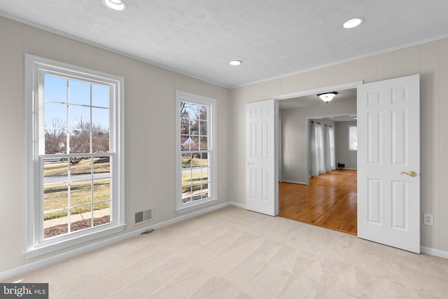 unfurnished room featuring a textured ceiling, carpet floors, visible vents, and crown molding