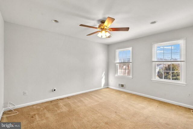 spare room featuring baseboards, ceiling fan, visible vents, and light colored carpet