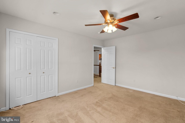 unfurnished bedroom with light carpet, a closet, a ceiling fan, and baseboards