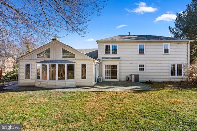 back of property featuring board and batten siding, a chimney, a yard, a patio area, and central AC