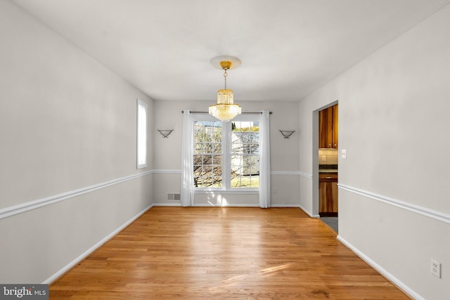 unfurnished dining area featuring baseboards, light wood-style flooring, visible vents, and a notable chandelier