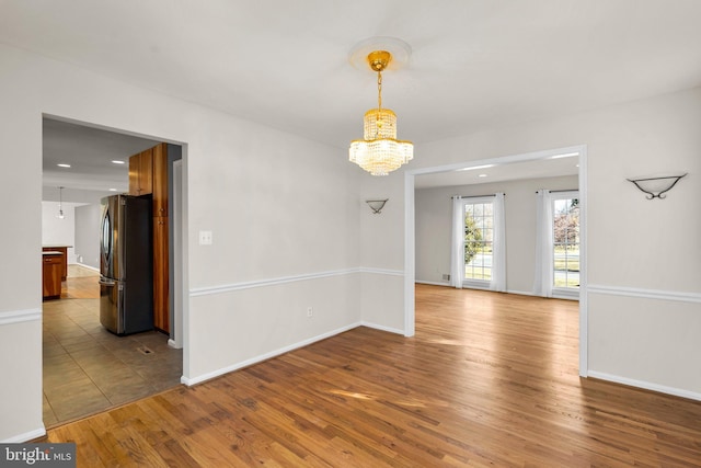 unfurnished room with baseboards, recessed lighting, wood finished floors, and an inviting chandelier