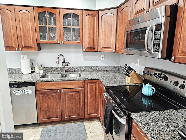 kitchen with a sink, light stone counters, appliances with stainless steel finishes, and brown cabinets