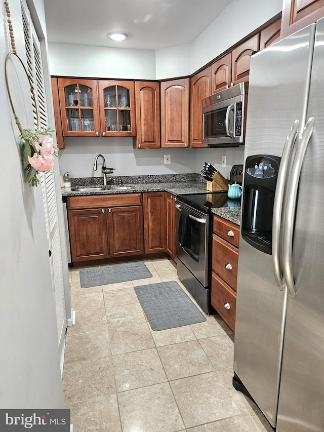 kitchen with a sink, stainless steel appliances, glass insert cabinets, and dark stone countertops