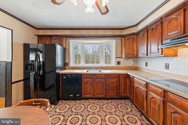 kitchen featuring wallpapered walls, a sink, light countertops, black appliances, and crown molding