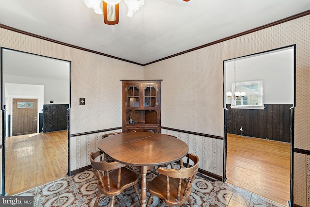 dining room with ceiling fan with notable chandelier, ornamental molding, wood finished floors, and wallpapered walls