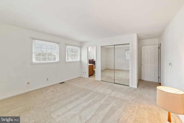 unfurnished bedroom with light carpet, baseboards, visible vents, ensuite bathroom, and a closet