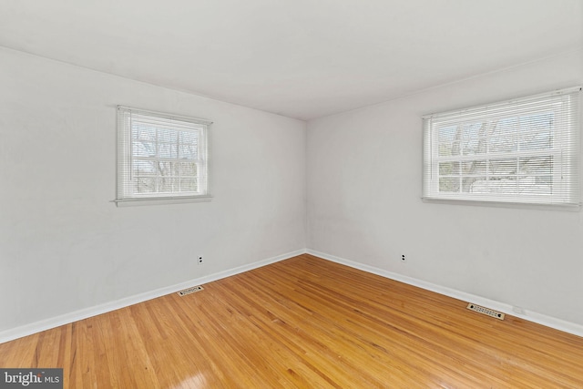 spare room with light wood finished floors, plenty of natural light, visible vents, and baseboards