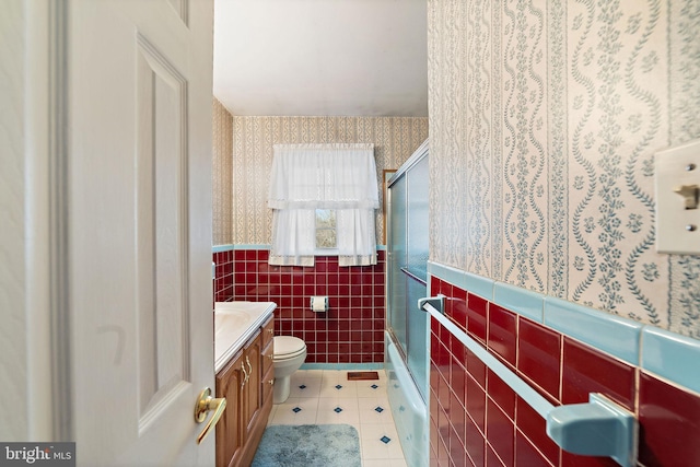 full bathroom with a wainscoted wall, tile walls, toilet, tile patterned flooring, and wallpapered walls