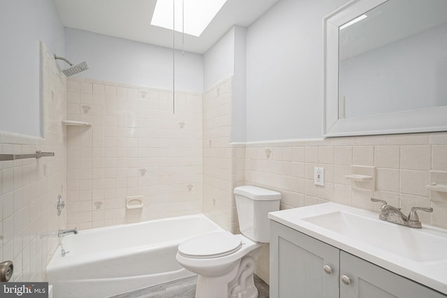 full bathroom featuring a skylight, a wainscoted wall, tile walls, shower / bathtub combination, and toilet