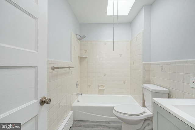 bathroom with a skylight, tile walls, toilet, vanity, and wood finished floors