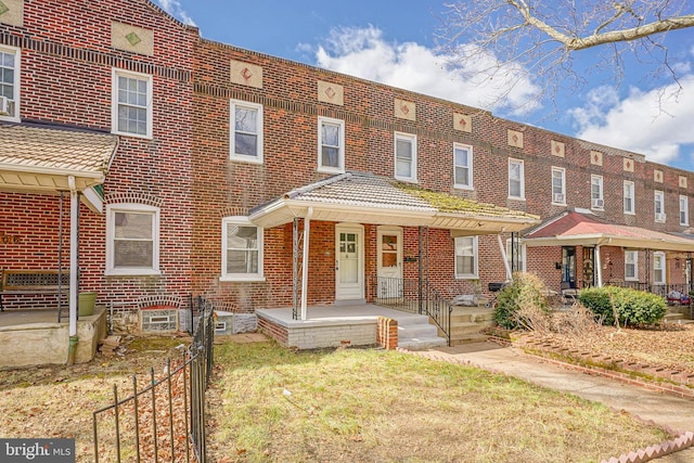 multi unit property with covered porch, a tiled roof, brick siding, and fence