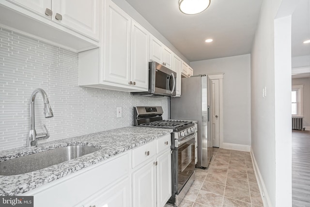 kitchen featuring white cabinets, radiator heating unit, a sink, stainless steel appliances, and backsplash